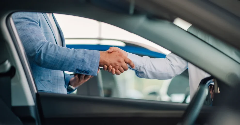 Verkäufer und Käufer geben sich Handschlag vor einem Auto
