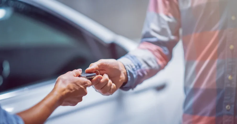 2 Menschen übergeben einen Autoschlüssel vor einem Auto
